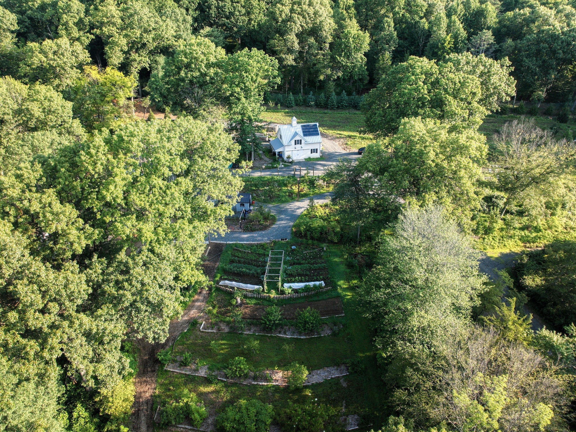 Aerial drone shot of Maranatha Farm showing barn, garden beds, solar panels, and winding driveway